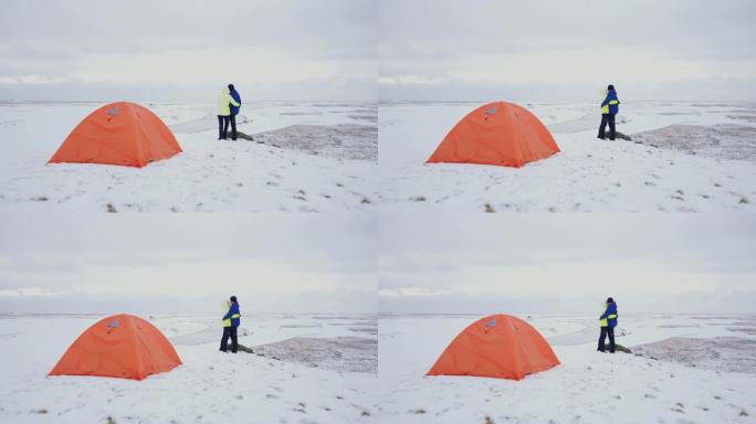 女士深情的夫妇在冰岛偏远的白雪覆盖的景观中拥抱露营帐篷