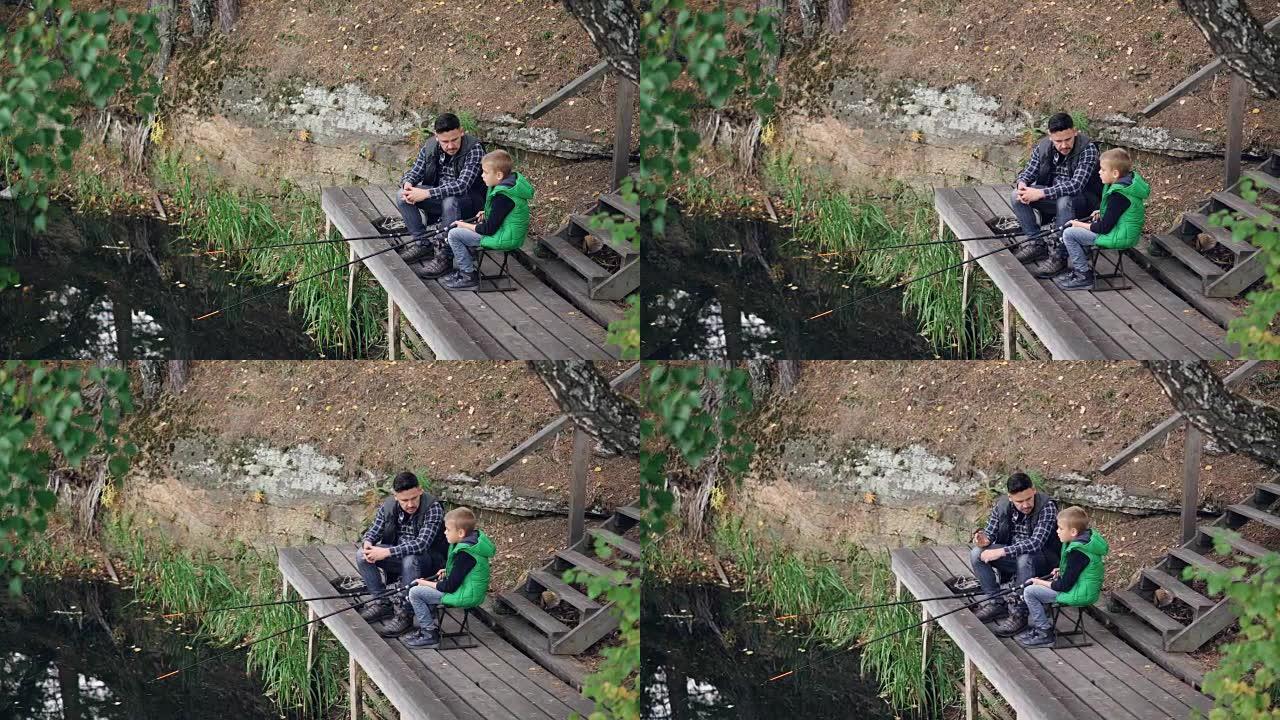 渔夫和他的孩子的高角度视图严肃的男孩从木制码头钓鱼，坐在椅子上的杆和说话。家庭、爱好、自然和关系概念