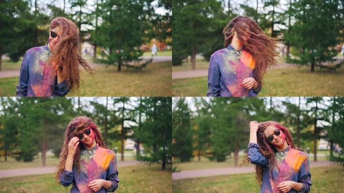 可爱的年轻女子学生的慢动作肖像在洒红节上玩得很开心，独自一人站在公园外面，把她的头发涂上五颜六色的粉