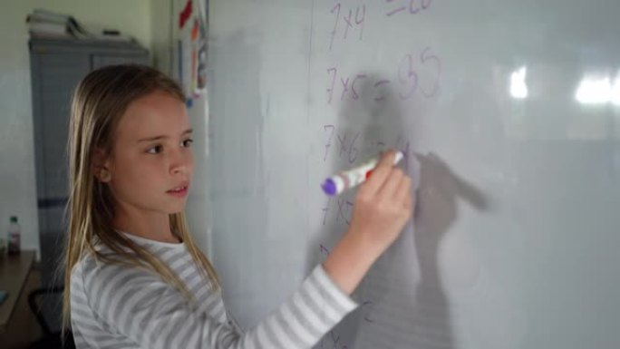 漂亮的小女孩在数学课上专注地在白板上写下答案