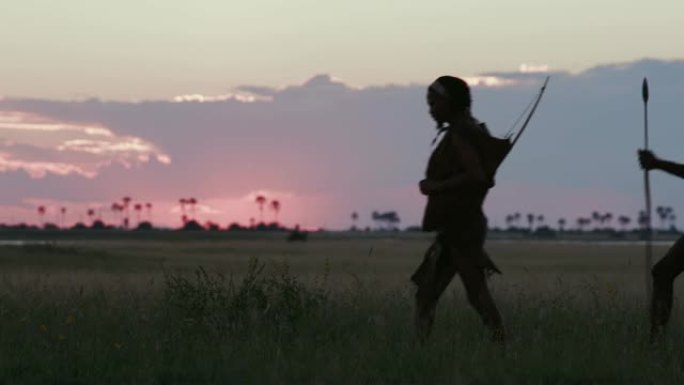 在博茨瓦纳的Makgadikgadi草原上，夕阳西下，三名桑族人/丛林人穿着传统服饰走过摄像机的4K