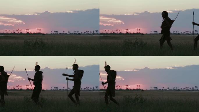 在博茨瓦纳的Makgadikgadi草原上，夕阳西下，三名桑族人/丛林人穿着传统服饰走过摄像机的4K