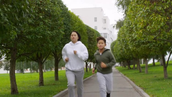 亚洲母亲和儿子带着树木沿着绿色小巷奔跑