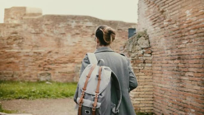 相机跟随年轻兴奋的旅行者女人，背着背包，在意大利奥斯蒂亚的古老历史红砖遗址上旅行。