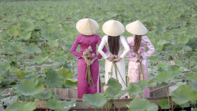 一个穿着越南民族服装或奥黛文化传统的年轻女子站在船上，在荷花花园里。越南