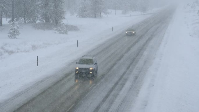 两辆汽车沿着一条冰冷的道路行驶，穿过被暴风雪困住的森林。