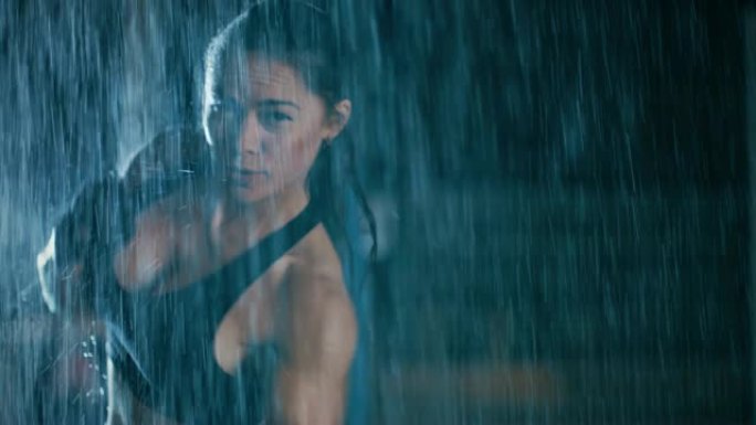 美丽的运动健身女孩正在做拳击运动。她晚上在大雨中锻炼身体，身后有一盏灯。