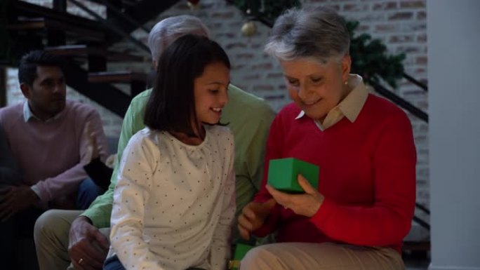 充满爱心的孙女在圣诞节期间拥抱和微笑时将礼物交给祖母
