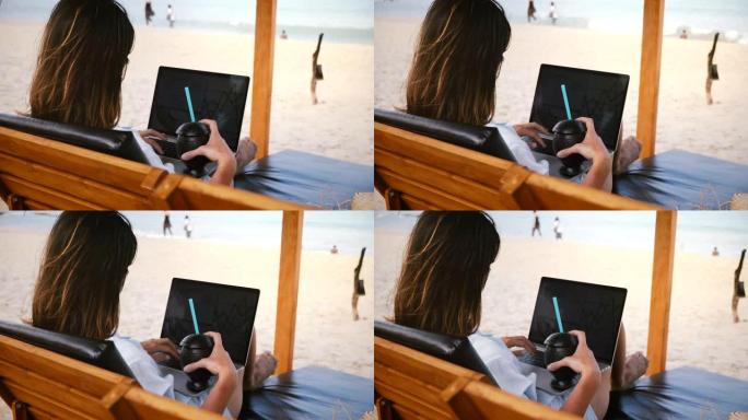 在风景秀丽的海洋海滩的躺椅上，成功的快乐自由职业者在笔记本电脑图表上喝酒。