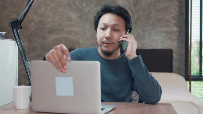 亚洲男子在家使用笔记本电脑和手机工作