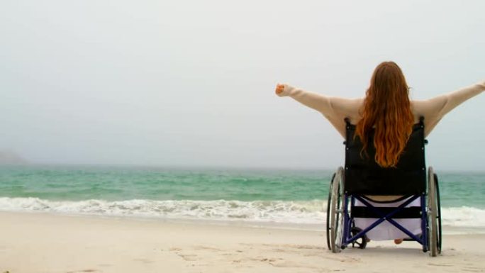 在海滩4kouple hav，年轻的白人妇女坐在轮椅上，双臂伸出