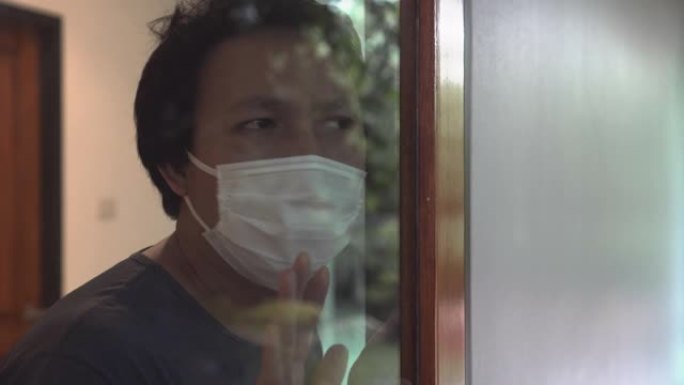 亚洲男子透过窗户自我检疫寻找冠状病毒或新型冠状病毒肺炎