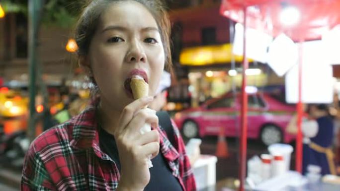 年轻迷人的亚洲女性晚上在夜市享受华夫饼蛋卷草莓冰淇淋。