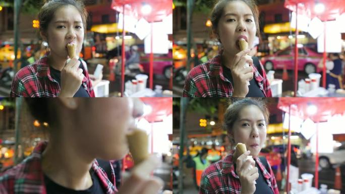 年轻迷人的亚洲女性晚上在夜市享受华夫饼蛋卷草莓冰淇淋。