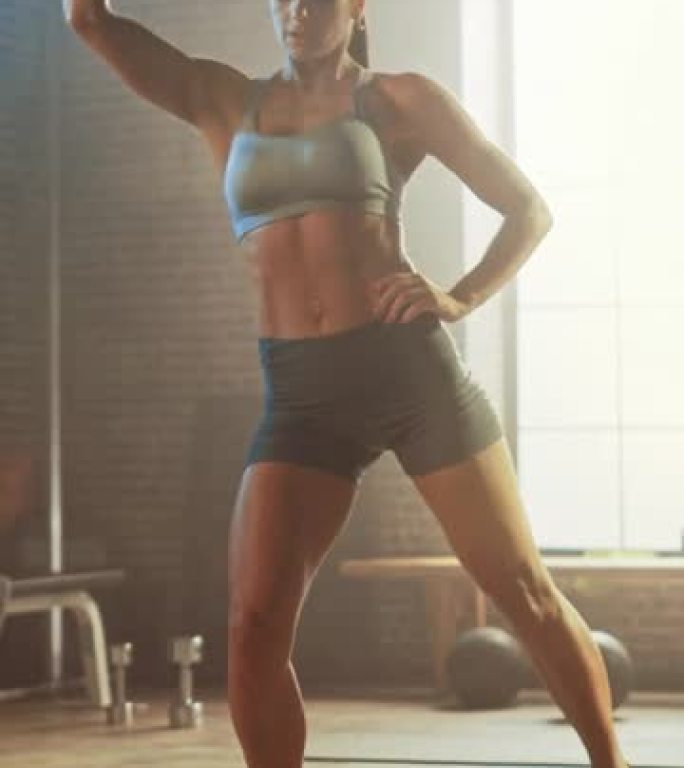强壮和适合美丽的运动女人在运动上衣和短裤是在一个阁楼风格的工业体操与动机海报做站立三月运动。垂直屏幕