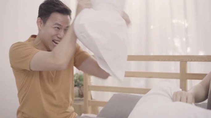 亚洲夫妇在卧室的床上玩枕头大战，妻子和丈夫躺在家里的床上享受有趣的时刻。情侣放松享受在家中的爱情时刻
