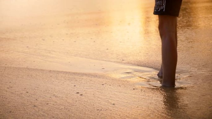 相机倾斜到快乐的小女孩身上，在异国情调的日落海滩上触摸潮湿的沙滩和泡沫波浪