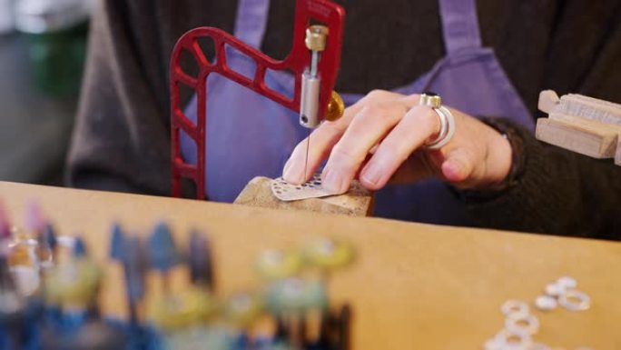在工作室里用锯子处理胸针的女性珠宝商的特写