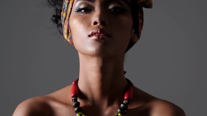 年轻漂亮的时尚模特，具有传统的非洲风格，深色背景上有围巾，耳环和化妆。黑色后台上深色皮肤模特的侧视图