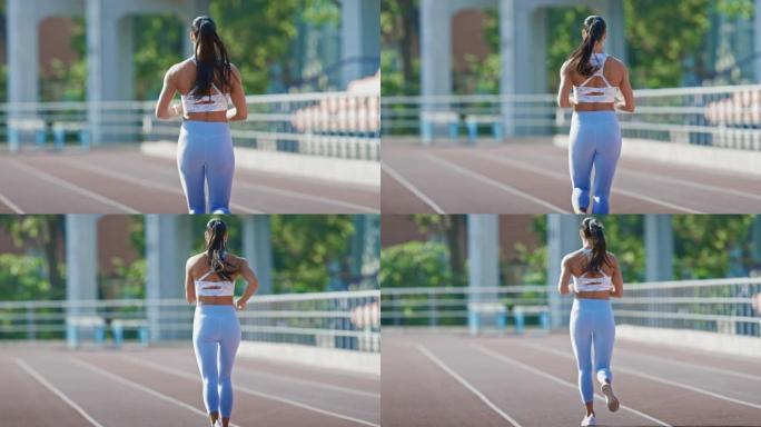穿着浅蓝色运动上衣和打底裤的美丽健身女子在体育场慢跑。她在一个温暖的夏日下午跑步。运动员在赛道上进行