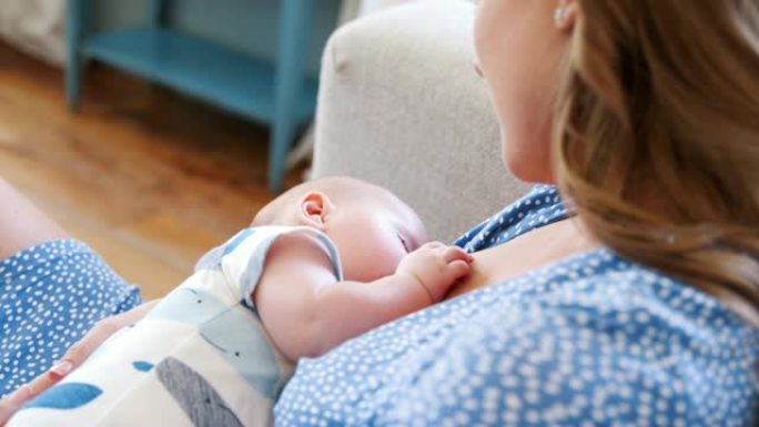 母亲坐在家里的沙发上母乳喂养的婴儿儿子的特写镜头-慢动作镜头