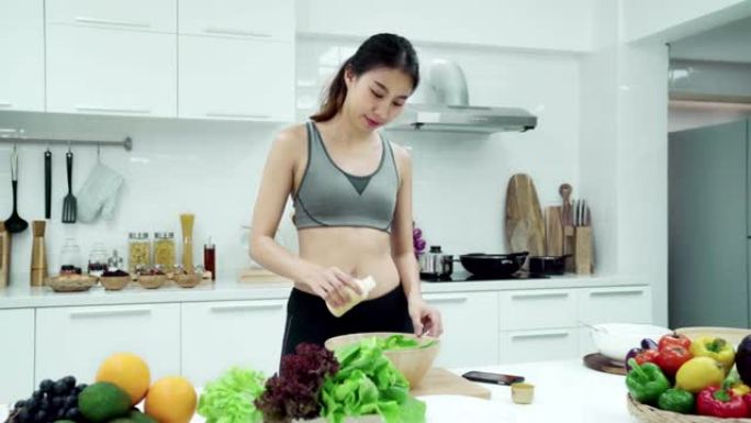 穿着运动服的亚洲女性在周末早上在厨房家里的智能手机上做沙拉和看食谱。健康饮食和健康生活方式理念。