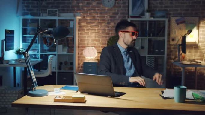 快乐的办公室工作人员戴着有趣的眼镜，用笔记本电脑在椅子上旋转