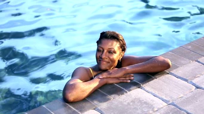 成熟的非洲裔美国妇女在游泳池里，挂在一边