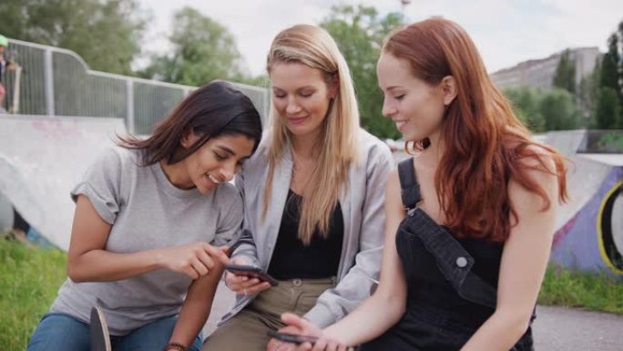 三个女性朋友在城市滑板公园看手机笑