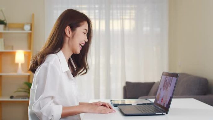 年轻的亚洲商界女性在客厅在家工作时使用笔记本电脑视频通话与家人爸爸和妈妈交谈。
