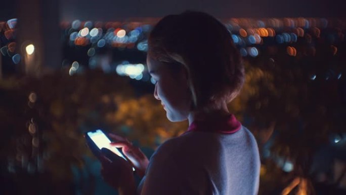 女性在夜间使用智能手机，旋转的bokeh背景