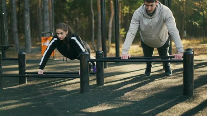 男女学生一起在户外锻炼，在低单杠上俯卧撑训练手臂和胸部肌肉。人和锻炼概念。