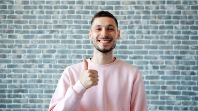 快乐男人的肖像在砖墙背景上露出竖起大拇指的微笑