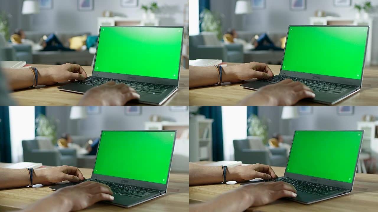在带有绿色模拟屏幕的笔记本电脑上，男人的手在肩膀上打字。背景舒适的客厅，女人在沙发上放松。