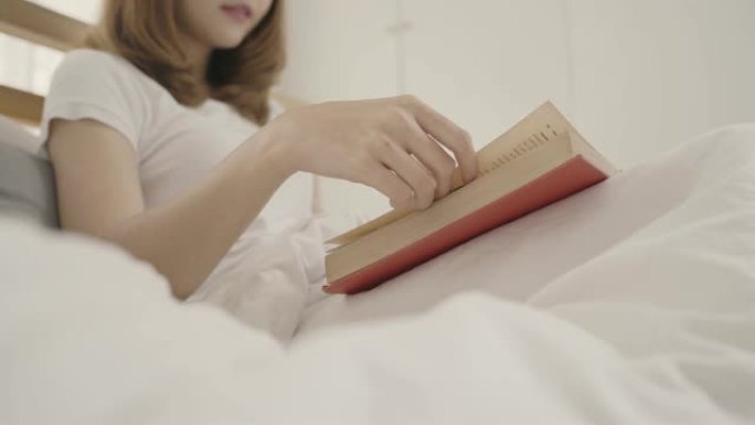 美丽的年轻亚洲女子躺在床上看书，女性睡觉后在家卧室放松。生活方式女性使用在家放松时间的概念。