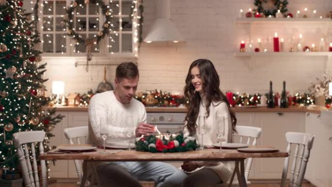 一对年轻夫妇正在为客人的到来准备圣诞晚餐。他们在客厅里摆放圣诞餐桌，点燃蜡烛。