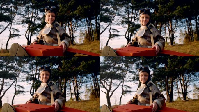 快乐的小飞行员男孩穿着纸板飞机服装站在树下，戴着老式眼镜玩飞行员慢动作。