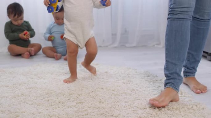 赤脚蹒跚学步的孩子在地毯上行走，三胞胎兄弟姐妹看着