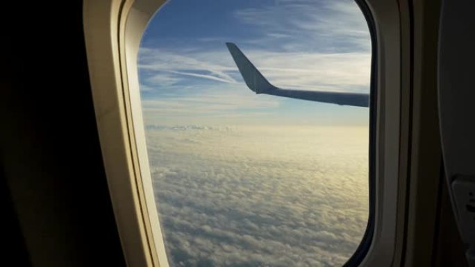 在飞行过程中从飞机舷窗拍摄视频。相机接近窗户，显示飞机如何在太阳照亮的软云面上方飞行。UHD