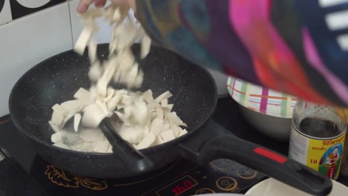 亚洲妇女在厨房的平底锅上手工煎豆腐。