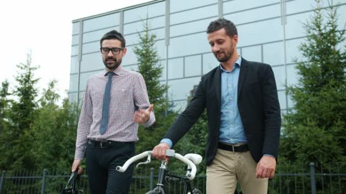 兴高采烈的商人带着自行车从办公室大楼里走来聊天