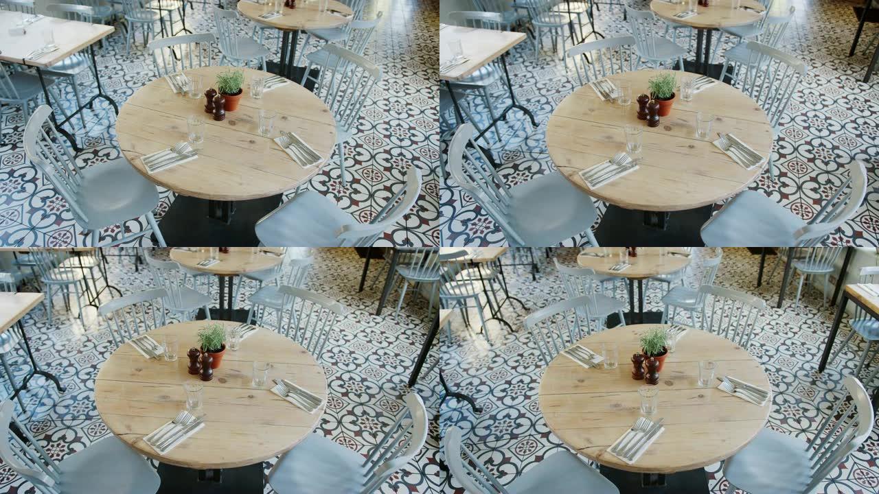 白天，高架手持视图集中在一张圆形木桌上，桌子上有地方设置和空餐厅餐厅里的椅子