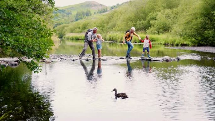 祖父母在英国湖区徒步旅行时帮助孙子过河的慢动作镜头