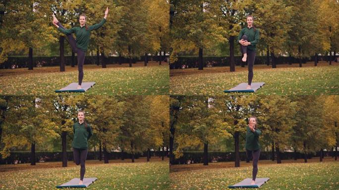 微笑女孩专业瑜伽教练正在公园草地上的垫子上单腿站立做平衡练习。美丽的秋天自然是可见的。