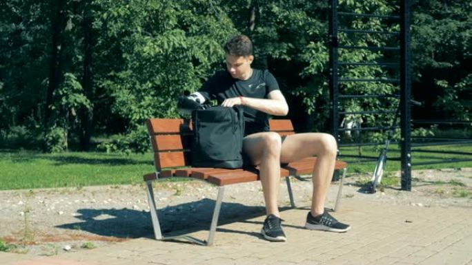 十几岁的少年坐在长凳上，用假手从包里拿出一台笔记本电脑。