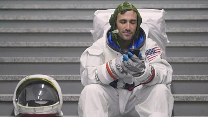 一名穿着衣服的宇航员使用智能手机打电话和发送信息。宇航员一边微笑，一边看着手中的电话。