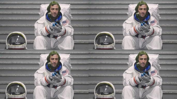 一名穿着衣服的宇航员使用智能手机打电话和发送信息。宇航员一边微笑，一边看着手中的电话。