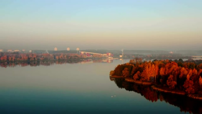 无人机高飞在美丽的城市天际线全景，日落湖森林与黄树。宁静的秋天自然。
