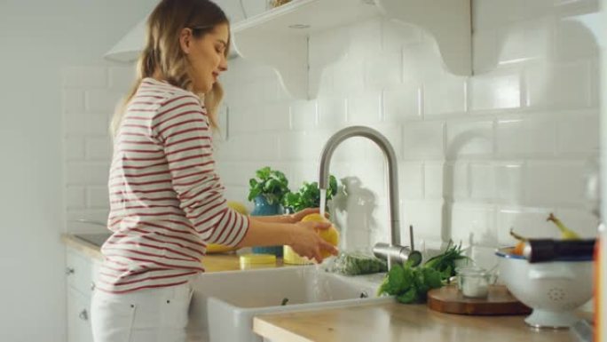 穿着条纹套头衫的美丽年轻女性正在厨房里洗甜椒和西红柿。明亮的白色现代厨房区。天然清洁饮食和健康的生活