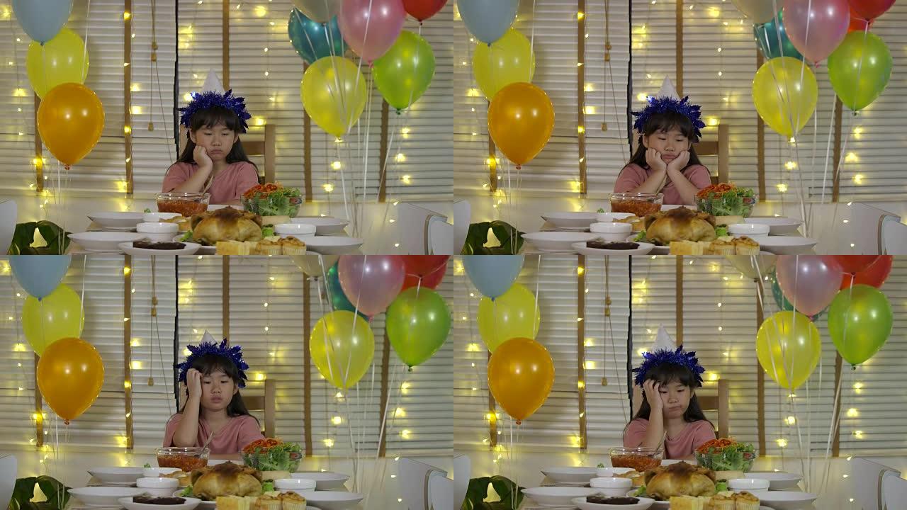 悲伤的亚洲小女孩独自在一张有蛋糕和蜡烛的桌子上庆祝她的生日，客人不来。慢动作。
